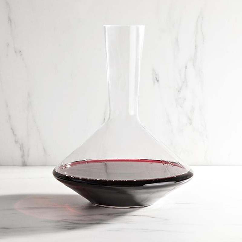 Decanter de cristal con vino tinto en su interior, colocado sobre una mesa sin copas.