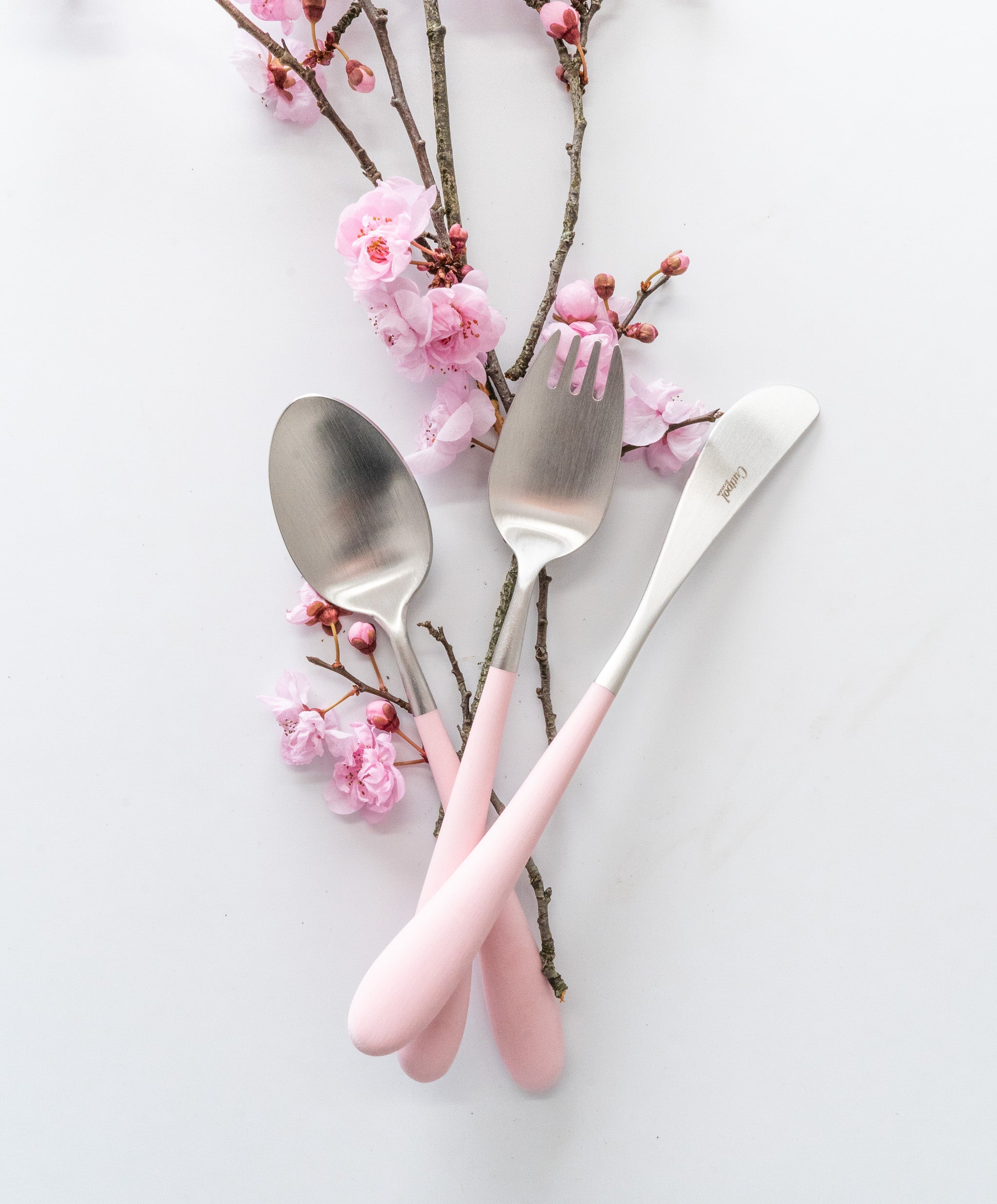 Set de cubiertos Cutipol Alice de 3 piezas, destacando el mango curvo de resina en color rosa y el acabado cepillado.