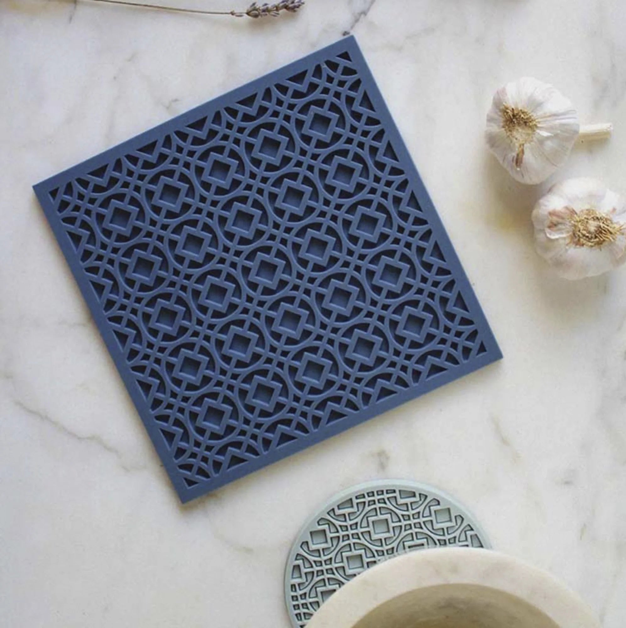 Portacalientes de silicona en forma de arabescos, de color azul, sobre una mesa de marmol.