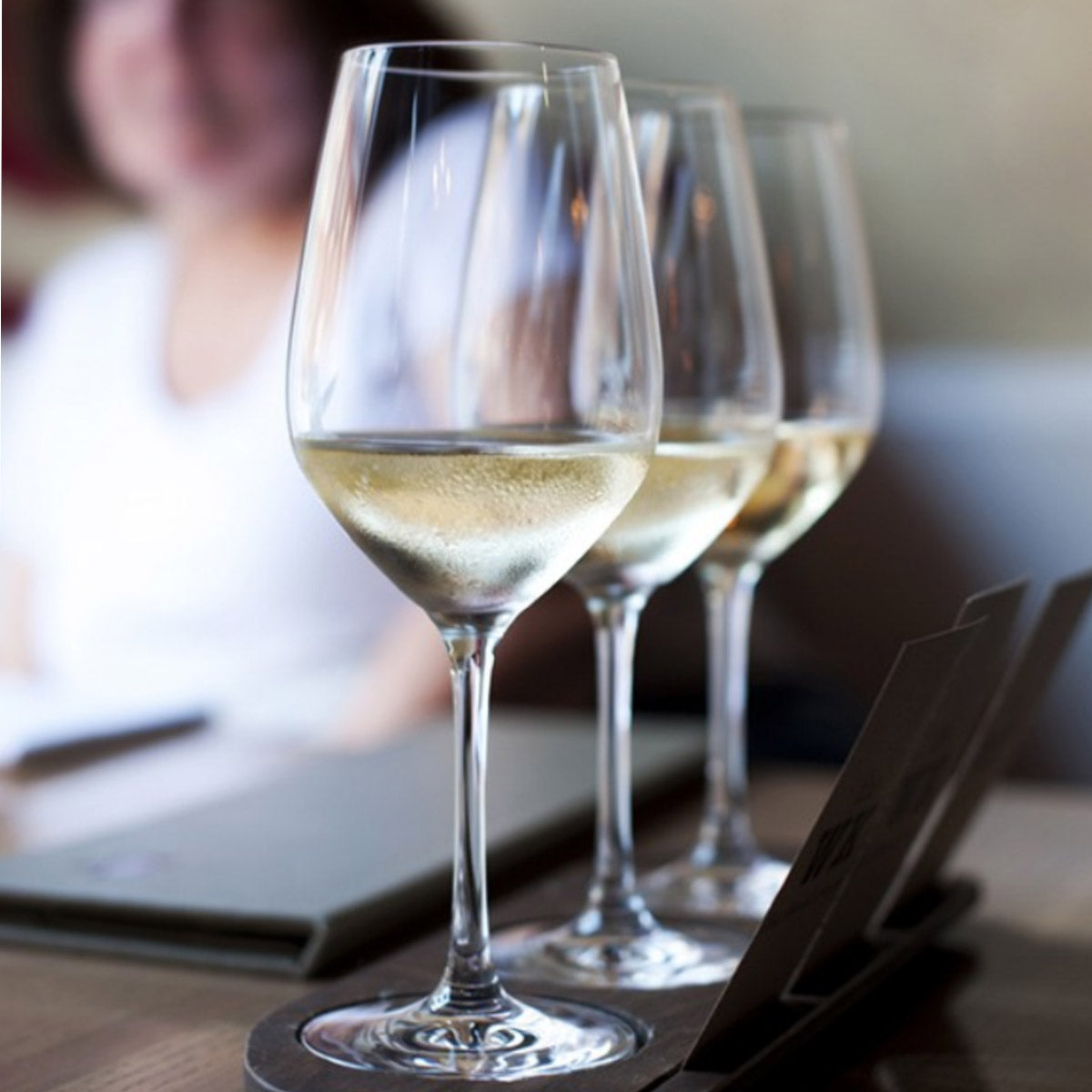 Primer plano de unas copas de vino blanco con el vino en su interior, mostrando su claridad y el reflejo de la luz.