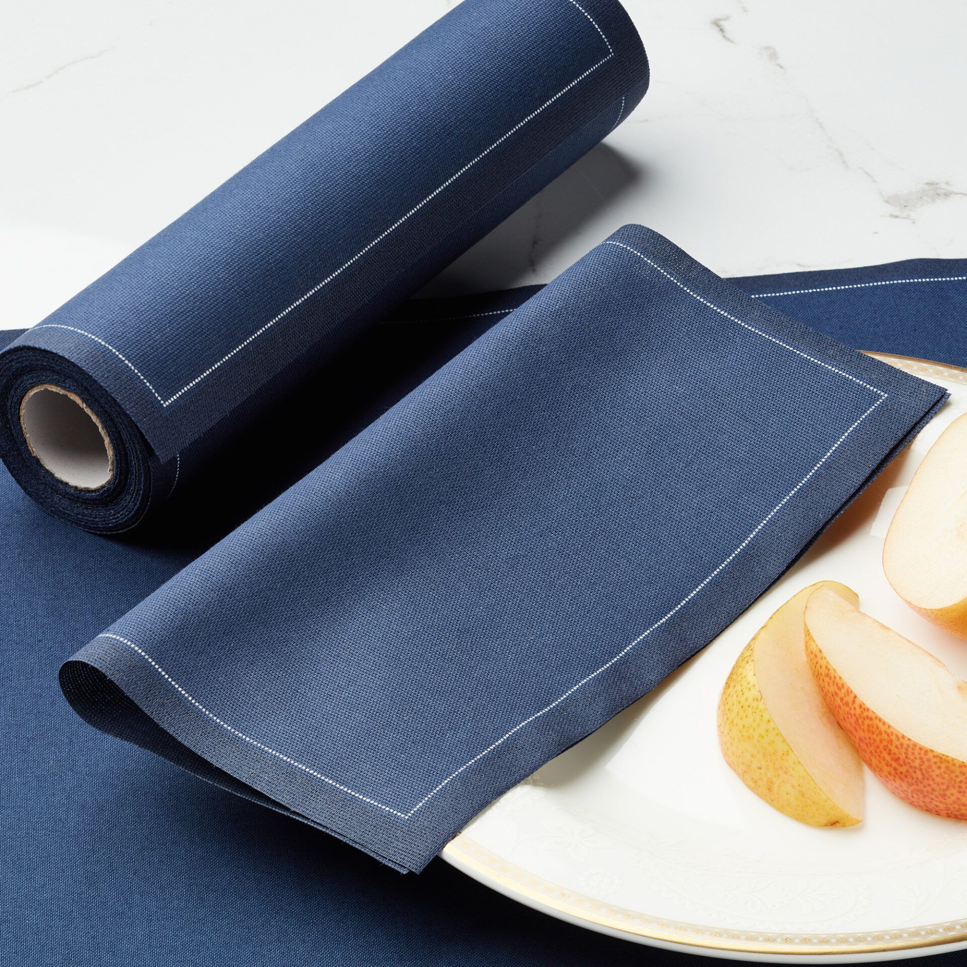 Servilletas My Drap de color azul sobre una mesa de cristal con platos y cubiertos, mostrando una puesta de mesa elegante.