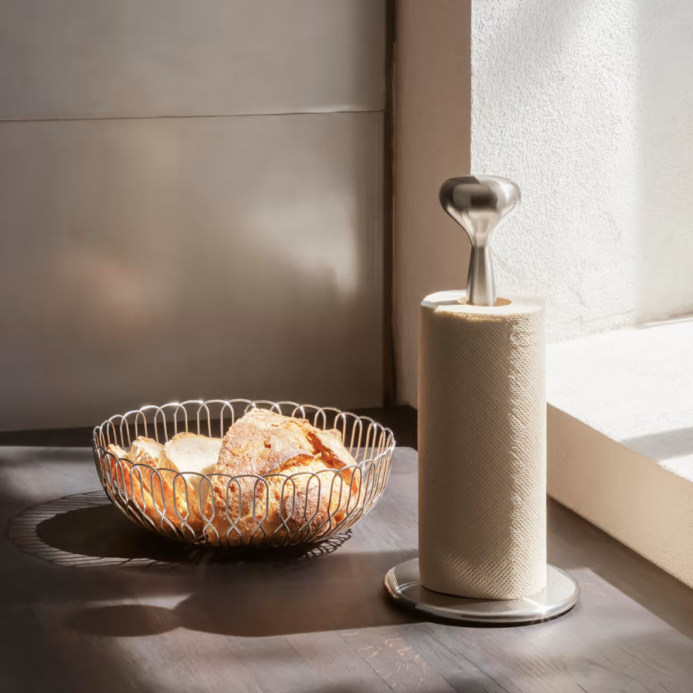 La canasta grande Alfredo de Georg Jensen dispuesta con baguettes y panes artesanales al centro de una mesa de desayuno contemporánea.