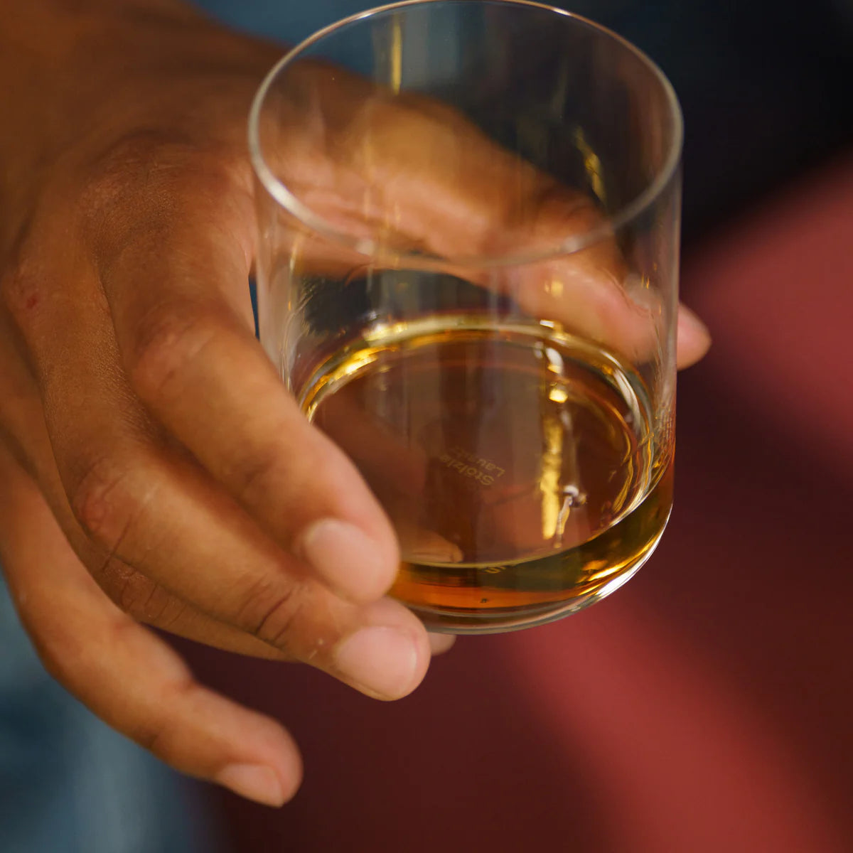 Vaso Whisky Kyoto de Stolzle Lausitz lleno de whisky, listo para degustar, con un fondo de bar acogedor.