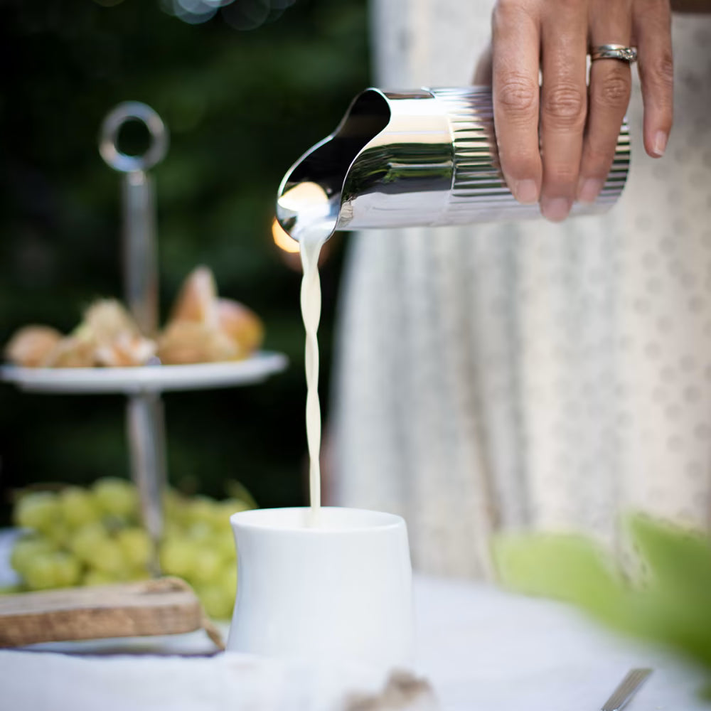 Fotografía de estilo de vida de la creamera Bernadotte, usada para servir leche en una taza de café.