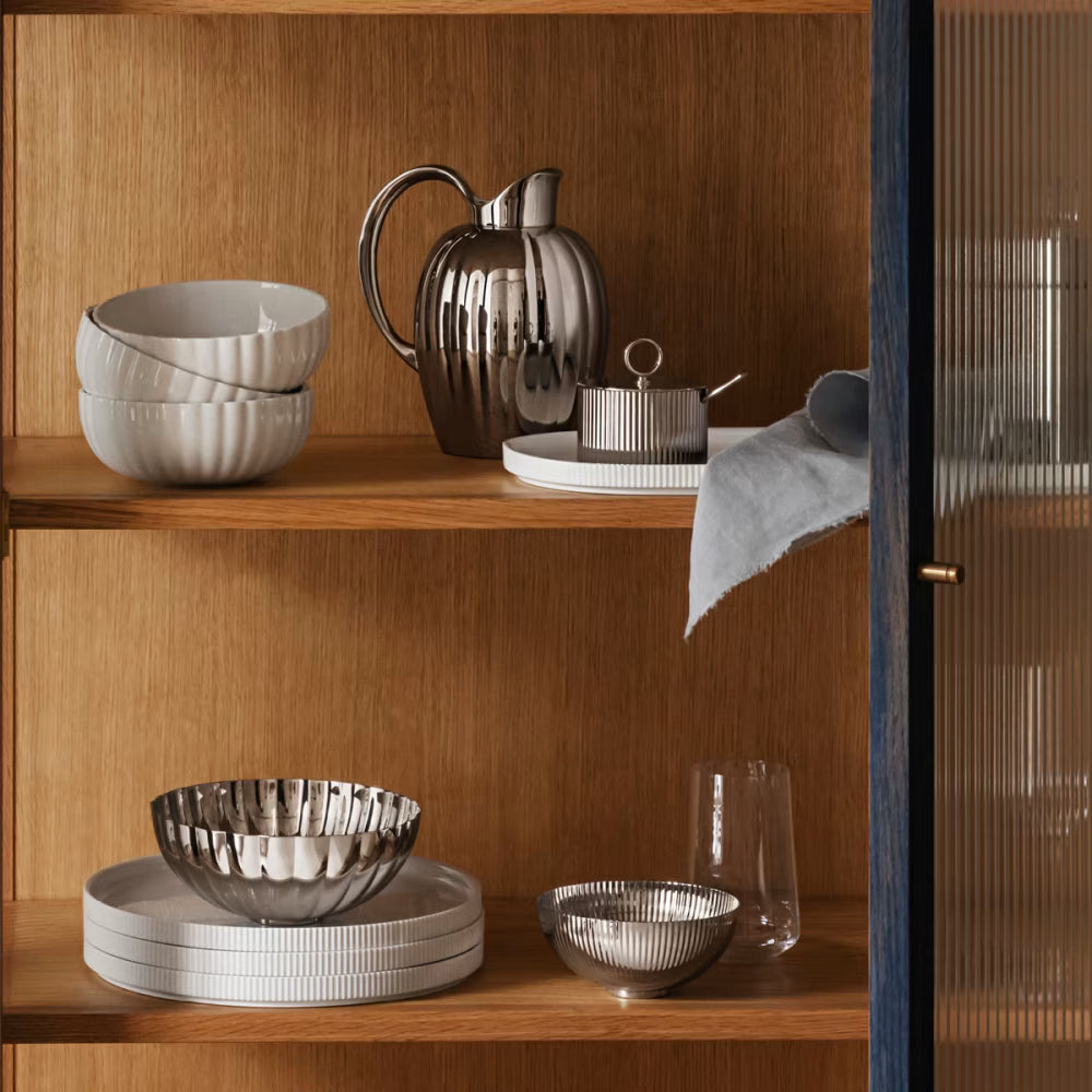 Plato principal Bernadotte de Georg Jensen, mostrando el diseño apilable estriado y blanco en una alacena.