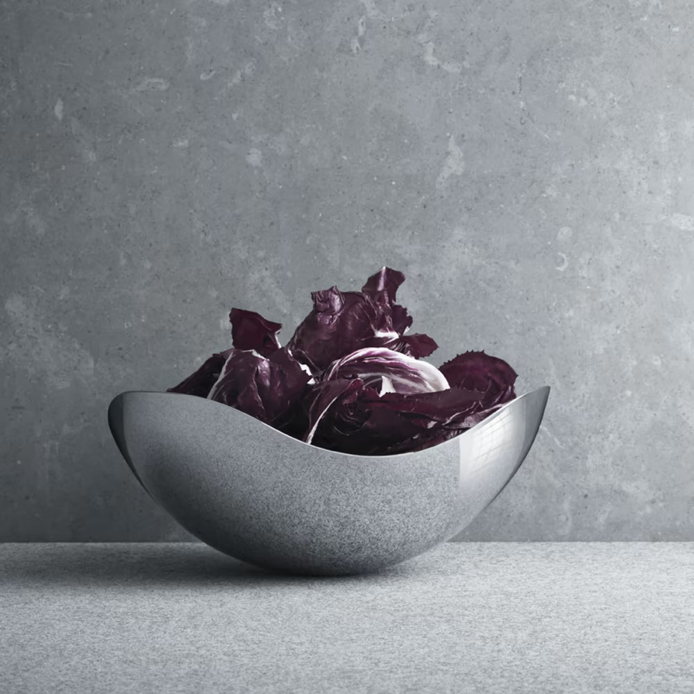 Bowl pequeño Bloom de Georg Jensen, mostrando el diseño curvo y pulido con ensalada en su interior.