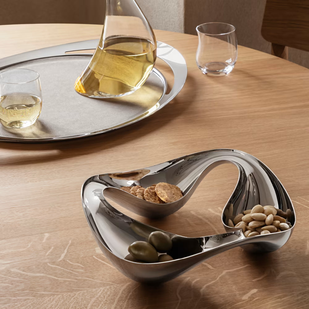 Bowl snack Cobra de Georg Jensen, mostrando el diseño curvo y pulido con aperitivos en su interior.