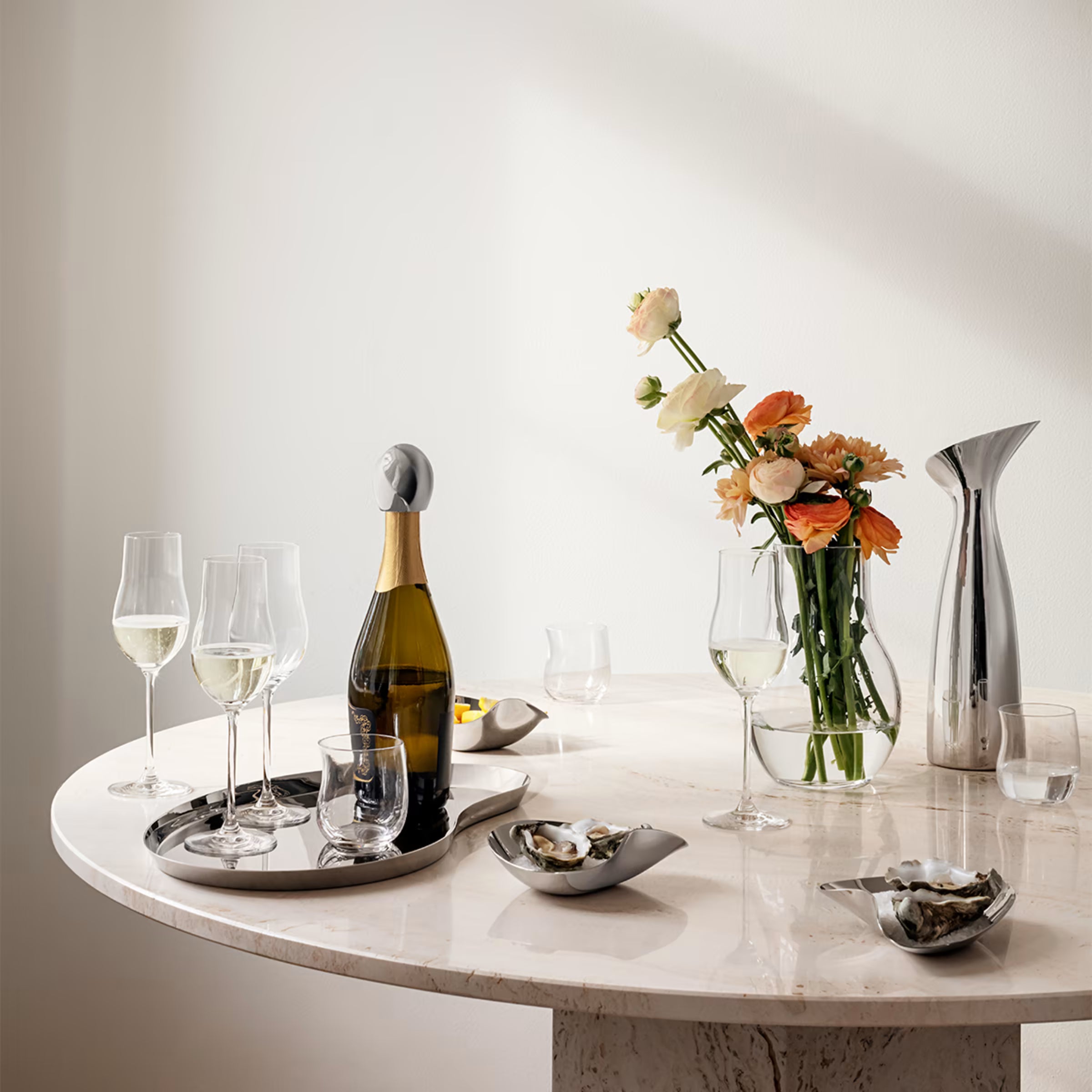 Una jarra Indulgence de Georg Jensen dispuesta de manera sofisticada sobre una mesa de comedor de mármol junto a copas de cristal