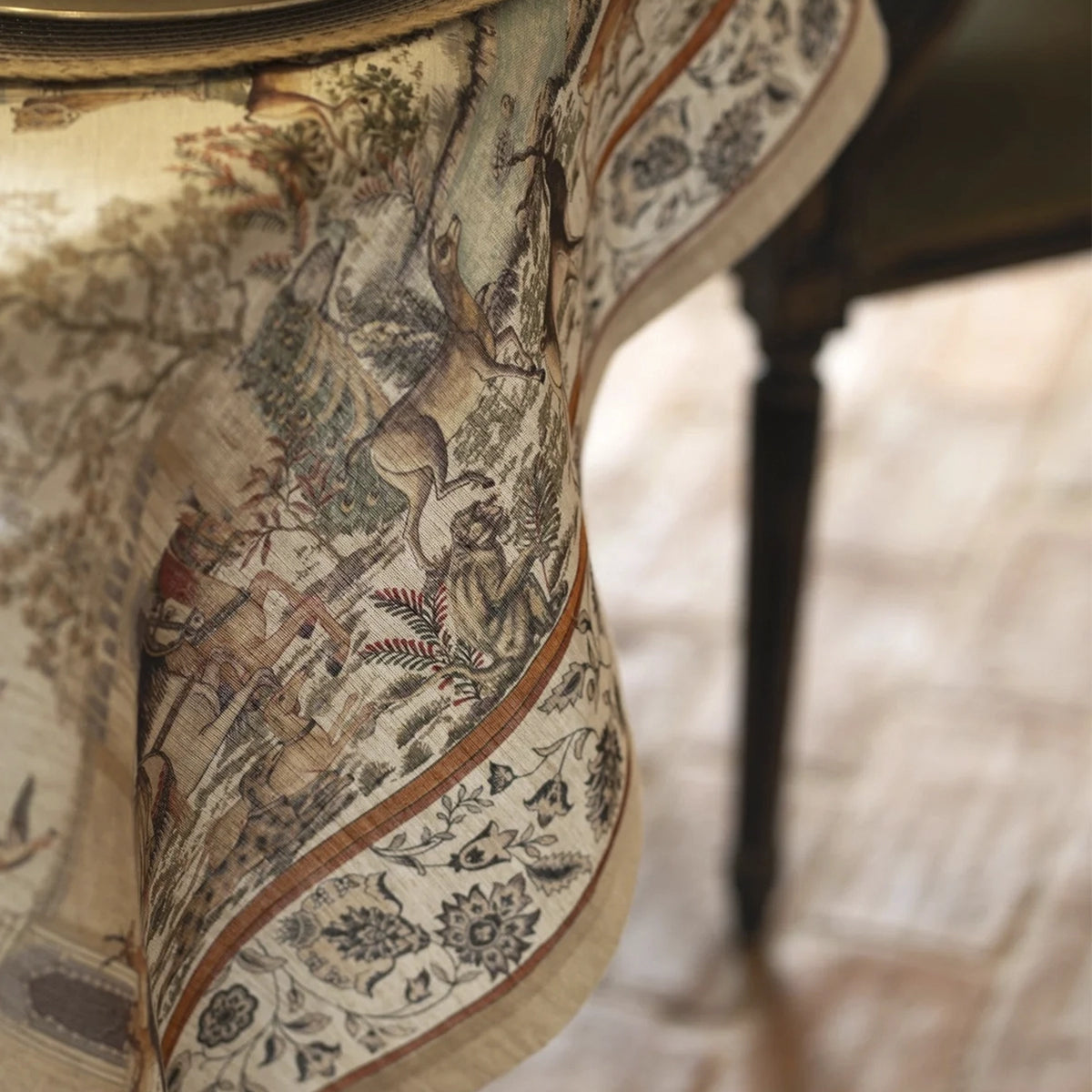 Primer plano de la trama del tejido de lino natural, los detalles de la ilustración oriental y el dobladillo perimetral del mantel Mudra de Tessitura Toscana Telerie.