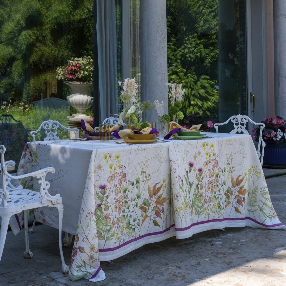 Mantel de lino Selvatica de Tessitura Toscana Telerie vistiendo una mesa de comedor elegante acompañado de vajilla fina y vasos de cristal.
