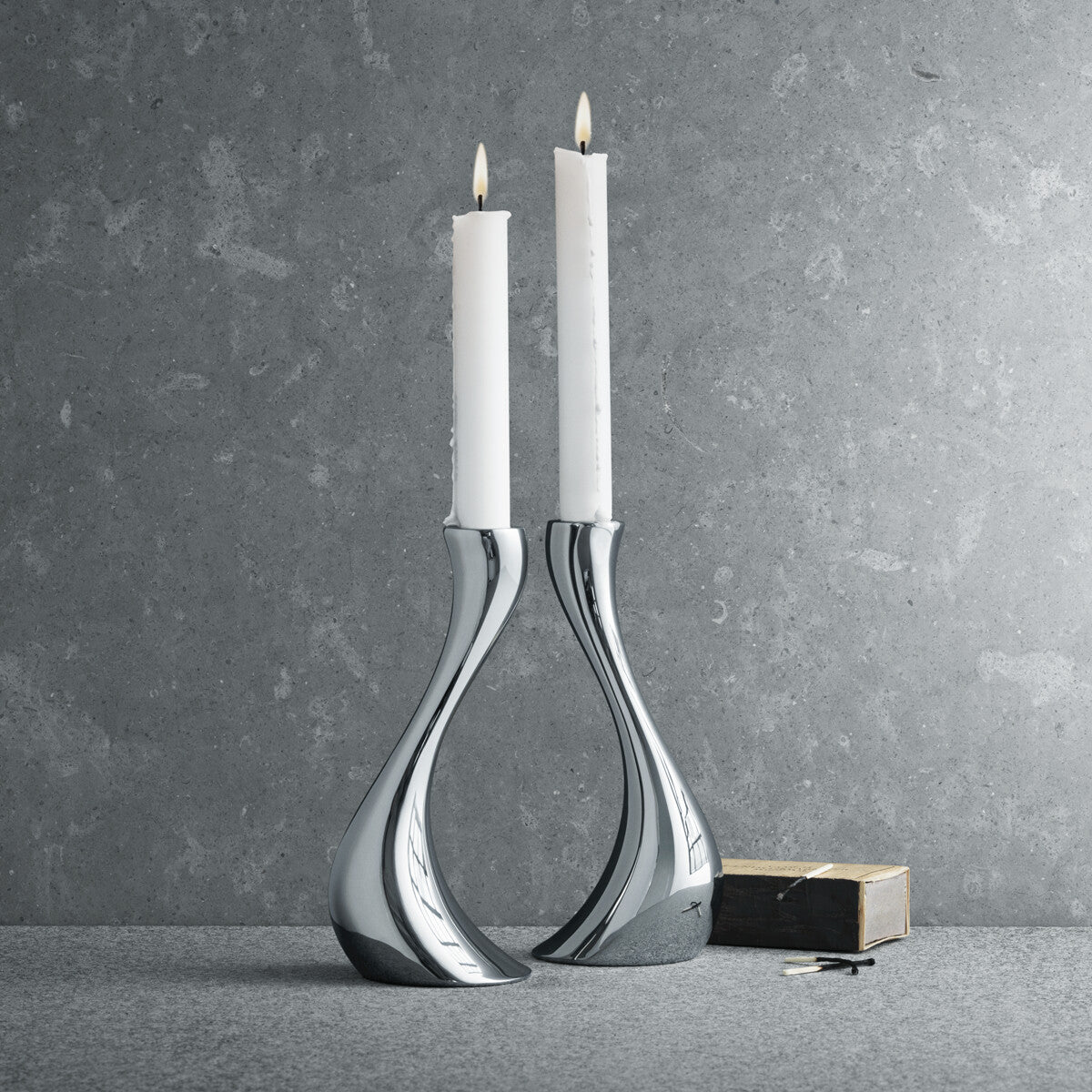 Candelabros Cobra, destacando el brillo del acero inoxidable pulido a espejo y la forma orgánica sobre un ambiente contemporaneo.