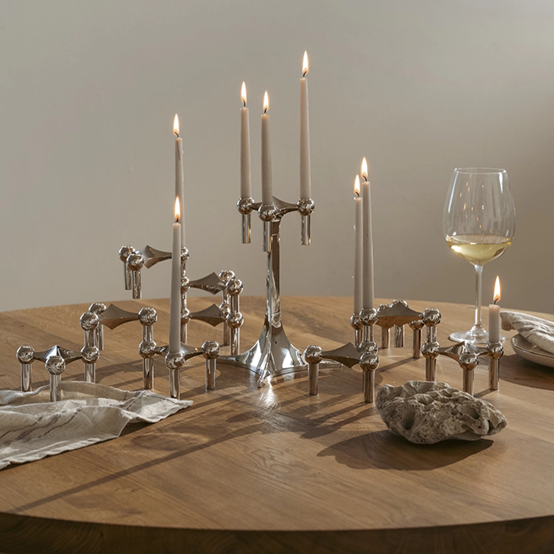 Set de candelabros cromados Nagel STOFF con velas cónicas encendidas.