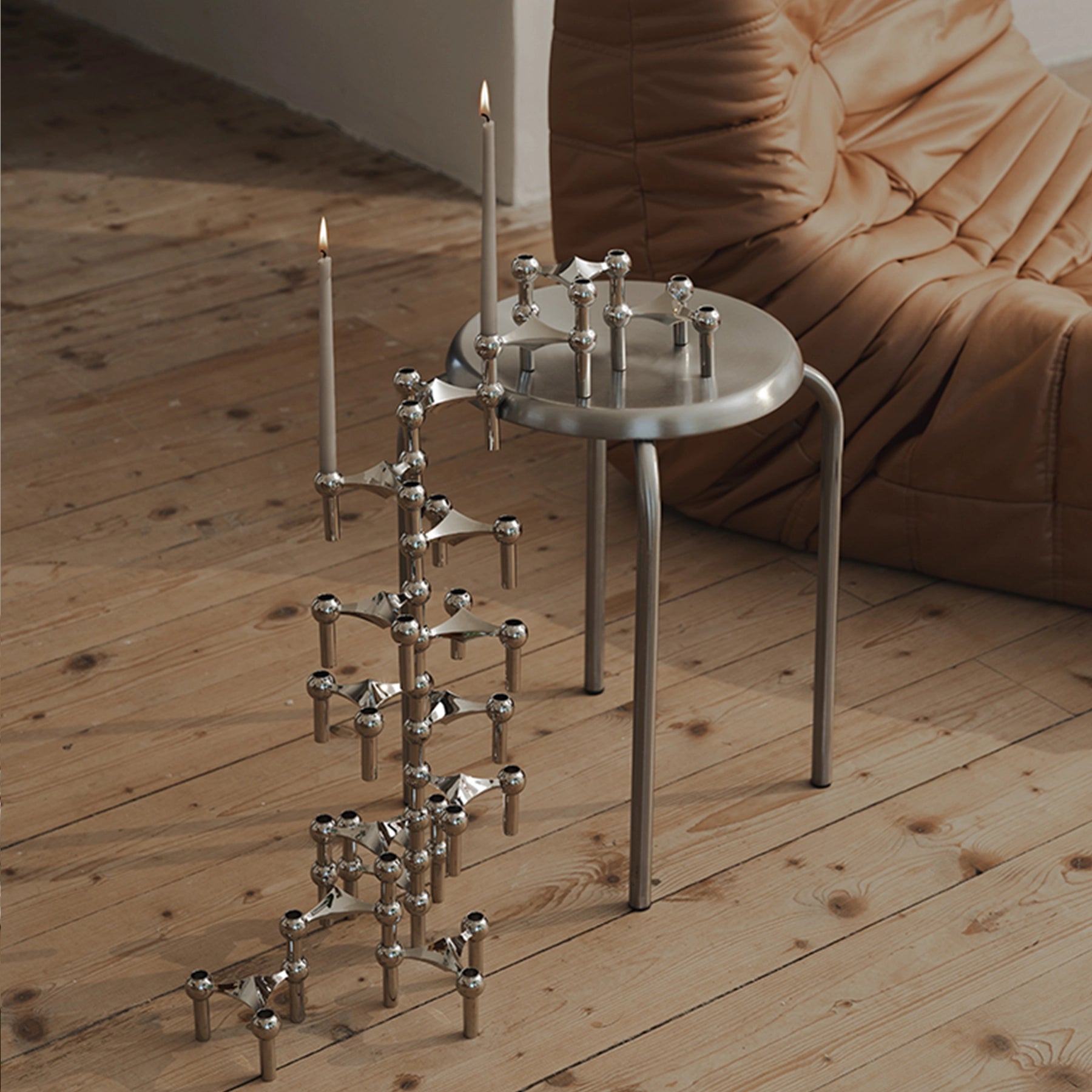 Set de candelabros cromados Nagel STOFF con velas cónicas encendidas.