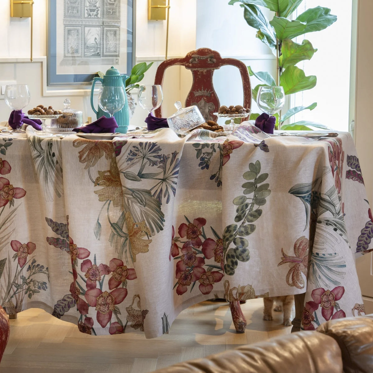 Mantel de lino Eradea Naturale de Tessitura Toscana Telerie vistiendo una mesa de comedor con vajilla de porcelana y copas de cristal en un almuerzo luminoso.