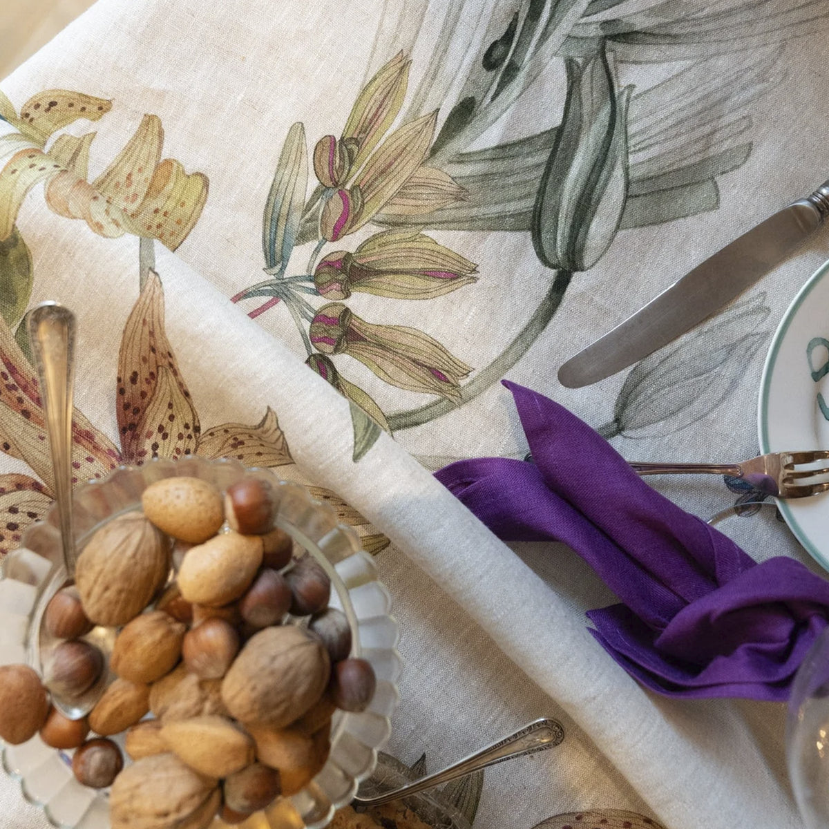 Primer plano de la textura del tejido de lino en color crudo y los detalles de las flores silvestres del mantel Eradea de Tessitura Toscana Telerie.
