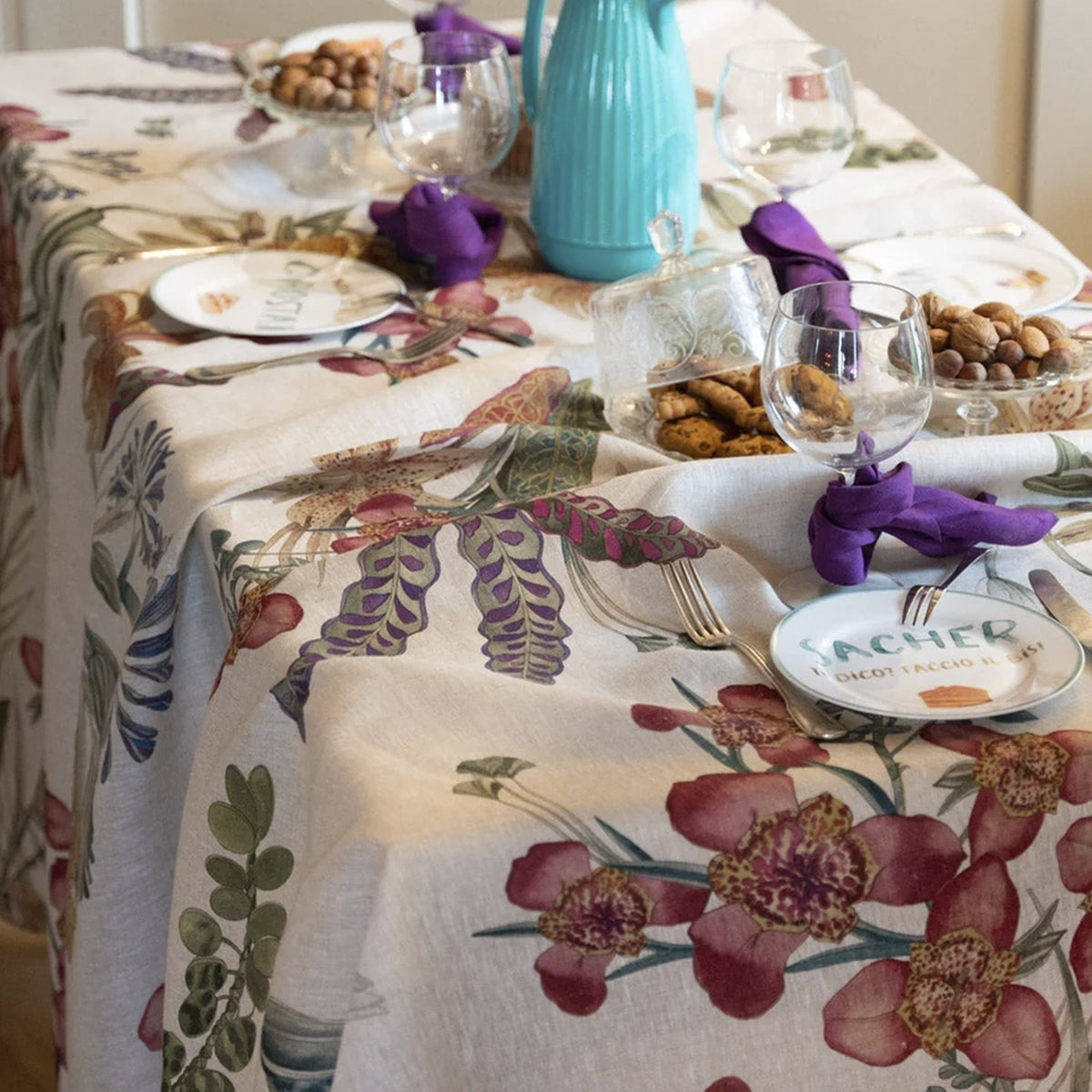 Mantel de lino Eradea Naturale de Tessitura Toscana Telerie vistiendo una mesa de comedor con vajilla de porcelana y copas de cristal en un almuerzo luminoso.