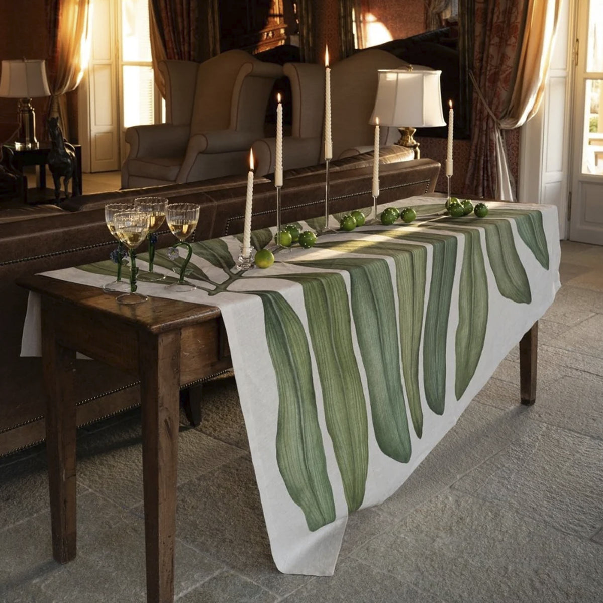 Mantel de lino Tamarindo de Tessitura Toscana Telerie vistiendo una mesa de comedor de verano con copas de cristal y cubiertos elegantes.